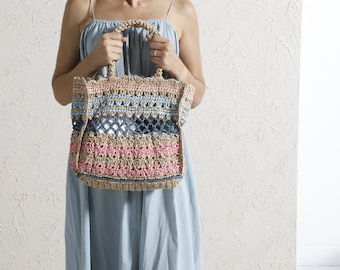 May include: A large, crocheted tote bag with a light brown base and colorful stripes of pink, blue, and light blue. The bag has a woven design and a wide, open top.