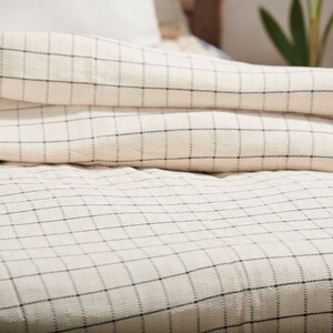 May include: A white and black checkered duvet cover with a subtle texture. The duvet is folded back to reveal the checkered pattern.