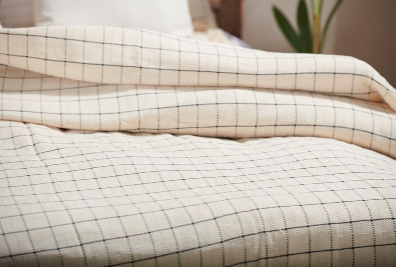 May include: A white and black checkered duvet cover with a subtle texture. The duvet is folded back to reveal the checkered pattern.