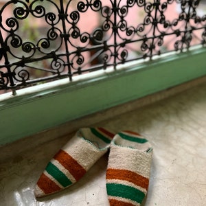May include: A pair of white, green, and brown striped slippers with pointed toes.