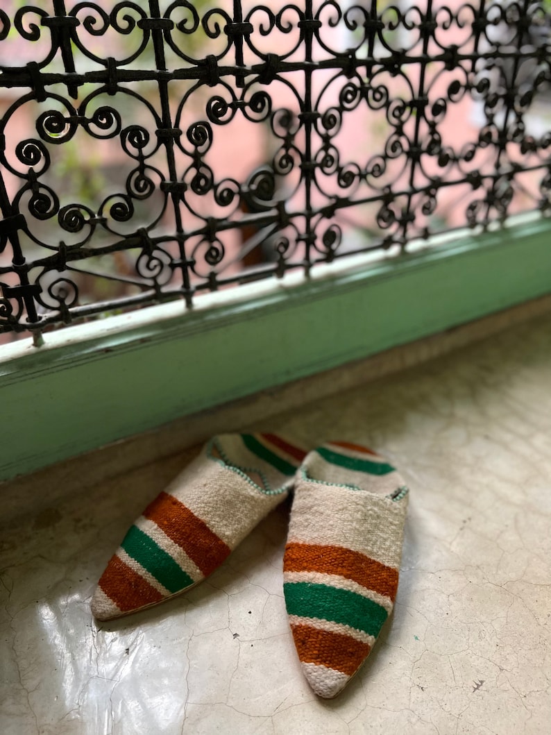 May include: A pair of white, green, and brown striped slippers with pointed toes.