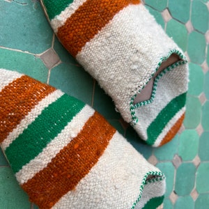 May include: A pair of white, green, and orange striped slippers. The slippers are made of a woven fabric and have a pointed toe.