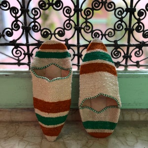 May include: A pair of white, orange, and green striped slippers. The slippers have a pointed toe and a flat sole.
