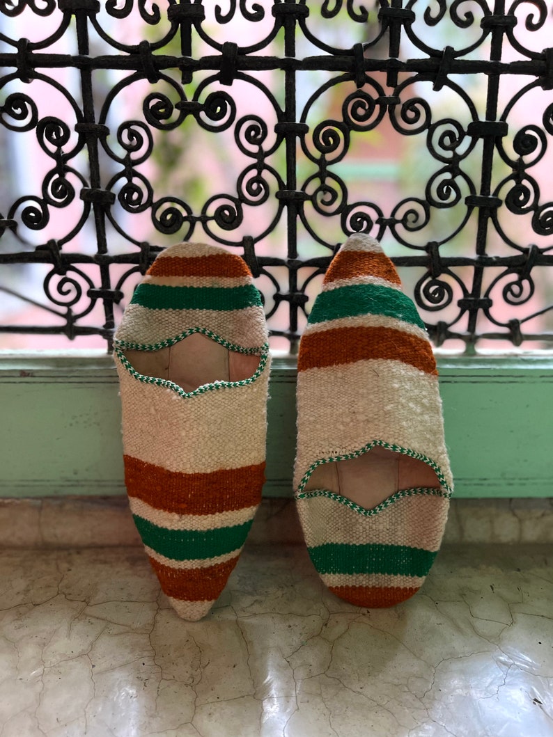 May include: A pair of white, orange, and green striped slippers. The slippers have a pointed toe and a flat sole.