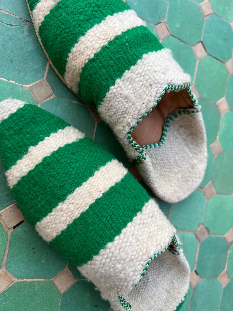May include: A pair of green and white striped slippers. The slippers are made of a soft, woven fabric and have a pointed toe.