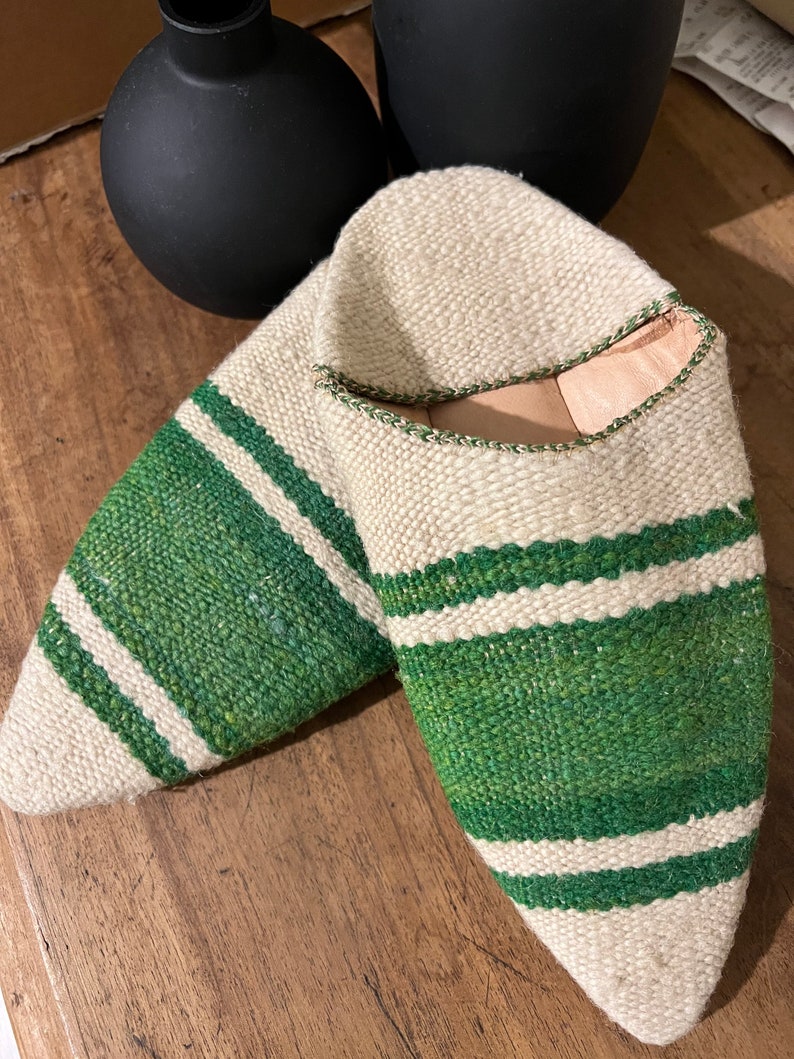 May include: A pair of white and green striped slippers. The slippers are made of woven fabric and have a pointed toe.