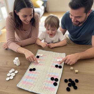 May include: A family plays a crochet backgammon game on a wooden table. The game board is cream-colored with pink and blue stripes. Black and white game pieces and two dice are also on the table. The family is smiling and pointing at the game.