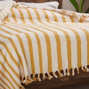 May include: A yellow and white striped throw blanket with tassels on the edges. The blanket is folded on a wooden bed frame.