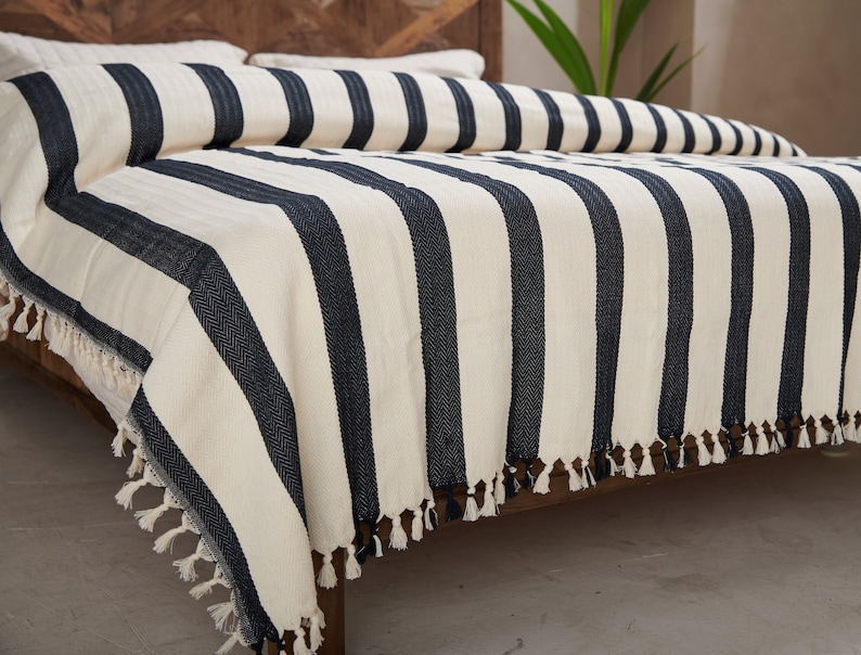 May include: A white and black striped throw blanket with fringe on the edges. The blanket is draped over a bed.