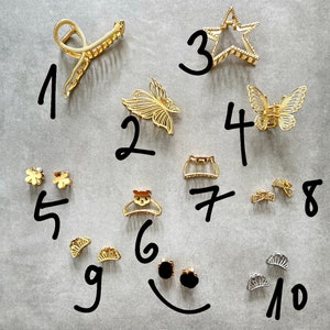 Pu&ograve; includere: Un set di dieci fermagli per capelli e accessori dorati, tra cui un fermaglio a forma di stella, fermagli a farfalla e piccoli fermagli a forma di fiore. I fermagli sono numerati da 1 a 10.