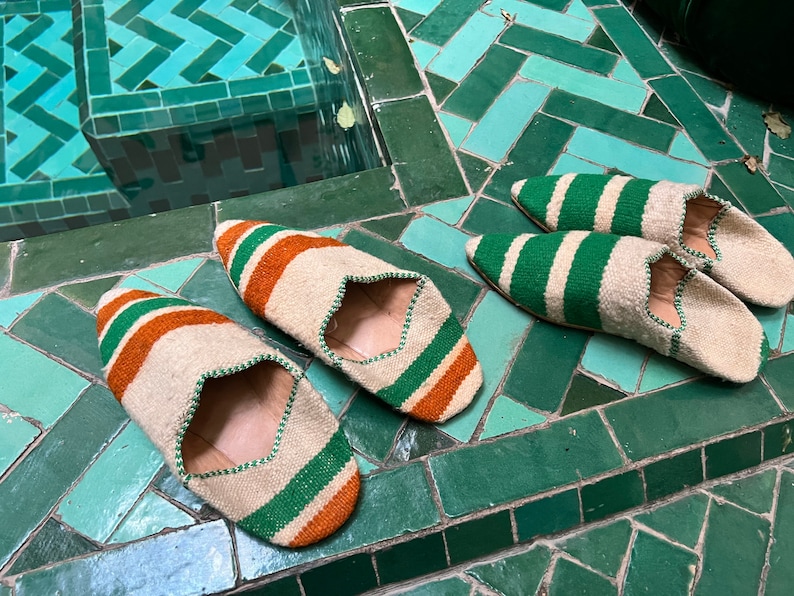 May include: Three pairs of woven slippers with green and orange stripes. The slippers are on a green tiled floor.