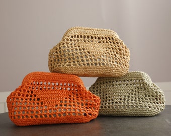 May include: Three crocheted bags in different colors: orange, beige, and green. The bags are made with a loose, open weave and have a rounded, slightly puffy shape.