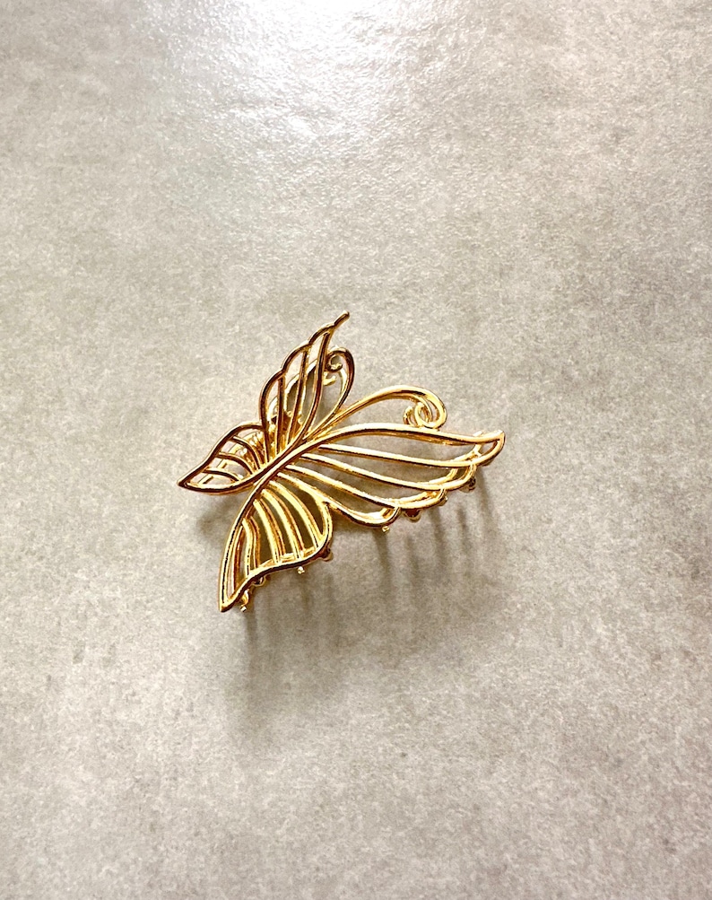 Pu&ograve; includere: Un fermaglio per capelli a forma di farfalla dorato con un design delicato e intricato. Il fermaglio ha una serie di denti sul fondo per tenere i capelli in posizione.