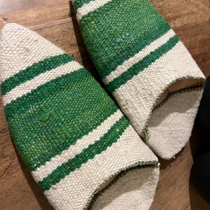 May include: A pair of white and green striped slippers. The slippers are made of a woven fabric and have a pointed toe.