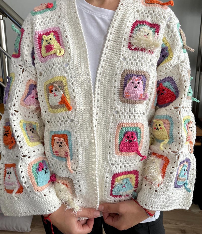 May include: White crochet cardigan with colorful cat appliques. The cardigan has a loose fit and a long sleeve. The cat appliques are crocheted in different colors and have a 3D effect.