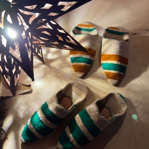 May include: A pair of green and white striped slippers with a pointed toe. The slippers are made of a soft, woven fabric and have a comfortable fit.