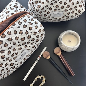 Può includere: Due pochette trapuntate con base bianca, motivo leopardato marrone e nero e cerniera marrone. Sono inclusi due pennelli per il trucco, una matita eyeliner bianca con la scritta Kess, una candela con motivo marmorizzato e un braccialetto.