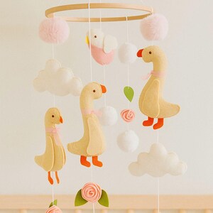 Pode incluir: Móvel de bebê feito à mão com gansos, nuvens e estrelas de feltro em tons pastel. O móvel inclui um aro de madeira, pompons rosa e elementos decorativos. Uma decoração encantadora para o berçário.