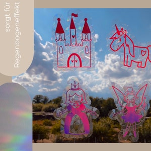 Könnte beinhalten: Vier schimmernde Aufkleber mit Regenbogeneffekt. Die Aufkleber zeigen ein rosa Schloss, ein rosa Einhorn, eine rosa Prinzessin und eine rosa Fee. Die Aufkleber befinden sich auf einem Fenster mit blauem Himmel und weißen Wolken im Hintergrund.
