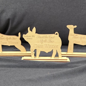 May include: Five wooden cutout animal silhouettes on individual bases. Each silhouette is a different animal, including a pig, a goat, a steer, a deer, and a cow. Each base has text that reads "Reserve Grand Champion Youth Steer", "Reserve Grand Champion Youth Goat", "Reserve Grand Champion Youth Pig", "Reserve Grand Champion Youth Deer", and "Reserve Grand Champion Youth Cow".