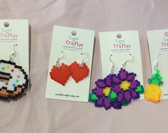 May include: Four pairs of handmade beaded earrings. The earrings are on cards with the text "Cami the Crafter". The earrings feature a donut, two hearts, a flower, and two pineapples.