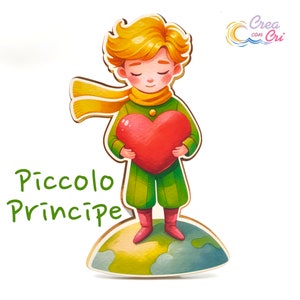 Può includere: Una statuetta di legno del Piccolo Principe che tiene un cuore rosso. La statuetta è in piedi su un piccolo pianeta rotondo verde e marrone. Il testo "Piccolo Principe" è scritto in verde sotto la statuetta.