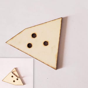 Op de afbeelding: Een houten, driehoekige broche met drie ronde gaten. De broche is lichtbeige met een donkerbruine rand. Een kleinere versie van de broche met een speldrug is ook afgebeeld.