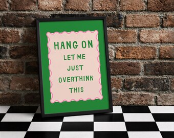 Könnte beinhalten: Ein gerahmter Kunstdruck mit dem Text "HANG ON LET ME JUST OVERTHINK THIS". Der grüne Text befindet sich auf einem rosa, wellenförmigen Hintergrund, der vor einem grünen Hintergrund steht. Der Rahmen ist schwarz, der Hintergrund eine Backsteinmauer und ein schwarz-weiß karierter Boden.