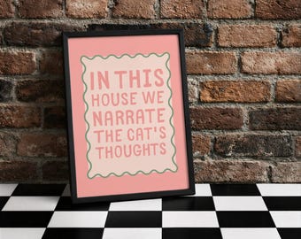 Könnte beinhalten: Gerahmter Kunstdruck mit dem Text "IN THIS HOUSE WE NARRATE THE CAT'S THOUGHTS" in Rosa und Grün. Der Druck befindet sich in einem schwarzen Rahmen und lehnt an einer Backsteinmauer. Der Boden ist schwarz-weiß kariert.