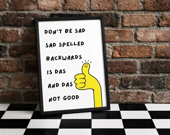 Könnte beinhalten: Ein gerahmter Druck mit dem Text "Don't be sad, sad spelled backwards is das and das not good." Der Druck hat einen schwarzen Rahmen und eine gelbe Daumen-hoch-Illustration. Der Hintergrund ist eine Backsteinmauer und ein schwarz-weiß karierter Boden.