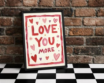 Könnte beinhalten: Ein gerahmter Kunstdruck mit den Worten "LOVE YOU MORE" in roter und rosa Schrift, umgeben von Herzen und Sternen. Das Kunstwerk ist vor einem cremefarbenen Hintergrund platziert und schwarz gerahmt. Der Druck wird auf einer schwarz-weiß karierten Oberfläche angezeigt.