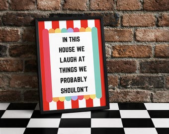 Könnte beinhalten: Gerahmtes Wandbild mit dem Text "IN THIS HOUSE WE LAUGH AT THINGS WE PROBABLY SHOULDN'T". Das Kunstwerk hat einen schwarzen Rahmen, einen weißen Hintergrund und farbenfrohe dekorative Ränder. Der Hintergrund ist eine Backsteinmauer und ein schwarz-weiß karierter Boden.