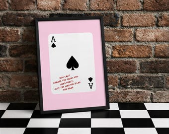 Könnte beinhalten: Gerahmter Druck mit einem Pik-Ass-Spielkarten-Design auf rosa Hintergrund. Die Karte hat schwarze Pik-Symbole und den Text "YOU CAN'T CHANGE THE CARDS YOU WERE DEALT. JUST THE WAY YOU PLAY THE HAND."
