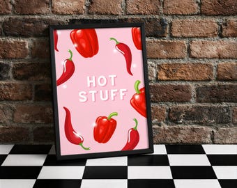 Könnte beinhalten: Ein gerahmter Druck mit rosa Hintergrund, der rote Chilischoten und Paprika zeigt. Die Worte "HOT STUFF" sind in Weiß gehalten. Der Druck befindet sich in einem schwarzen Rahmen, vor einer Backsteinmauer und einem schwarz-weiß karierten Boden.