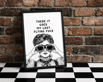 Puede incluir: Impresión artística enmarcada en negro con el texto "THERE IT GOES MY LAST FLYING FUCK". La ilustración en blanco y negro representa a una mujer sosteniendo unos prismáticos. La obra de arte se exhibe contra una pared de ladrillo y un suelo ajedrezado en blanco y negro.