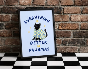 Puede incluir: Impresión artística enmarcada con un gato negro con pijama a cuadros azules y amarillos. El texto dice "Everything is better in pyjamas" en azul. El fondo es azul claro con estrellas amarillas. Marco negro.
