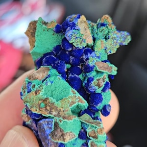 May include: A close-up of a mineral specimen with a striking colour palette. The piece displays a rich blue, contrasted by areas of vivid green and brown. The mineral's surface has a textured appearance, creating visual interest.