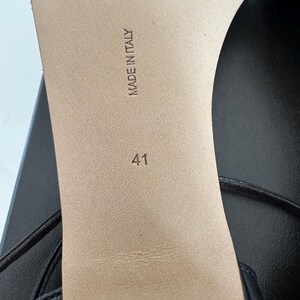 Peut inclure: Gros plan sur la semelle d'une sandale en cuir noir. Les mots "MADE IN ITALY" sont estampill&eacute;s sur la semelle int&eacute;rieure beige, ainsi que le num&eacute;ro "41". La sandale a un design &agrave; fines lani&egrave;res.