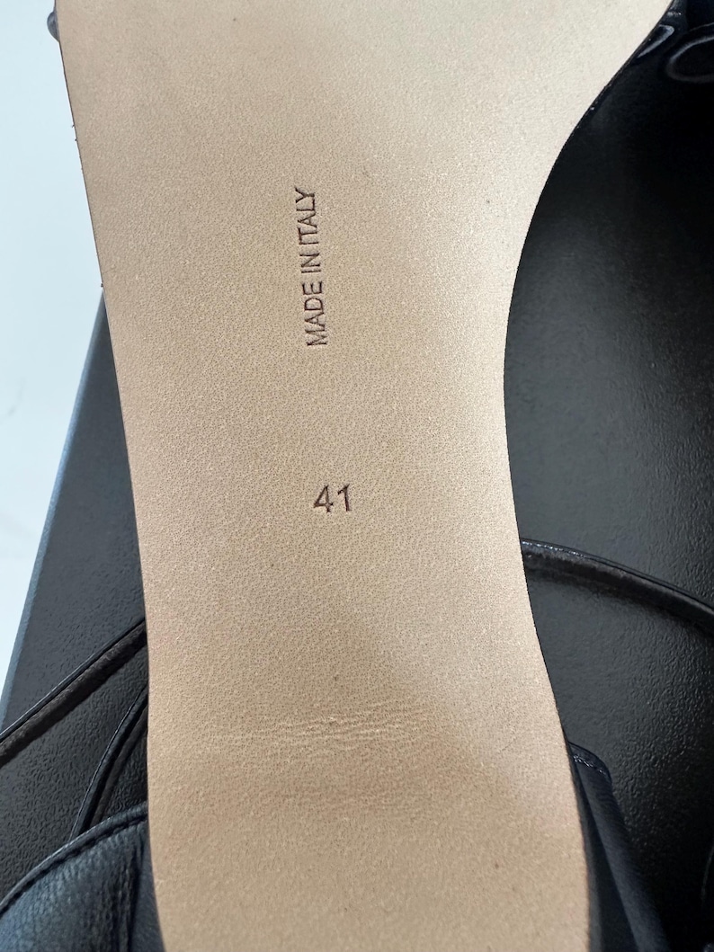 Peut inclure: Gros plan sur la semelle d'une sandale en cuir noir. Les mots "MADE IN ITALY" sont estampill&eacute;s sur la semelle int&eacute;rieure beige, ainsi que le num&eacute;ro "41". La sandale a un design &agrave; fines lani&egrave;res.