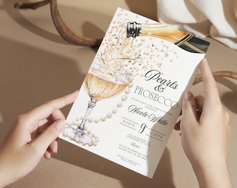 May include: A white invitation card with gold lettering for a bridal shower. The card features a watercolor illustration of a champagne flute with pearls and a bottle of champagne pouring into the glass. The text on the card reads "Pearls & Prosecco" and "Please join us for a bridal shower honoring Nicole White".