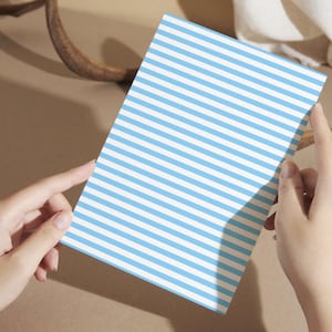 May include: A white card with blue horizontal stripes. The card is being held by a person's hands.