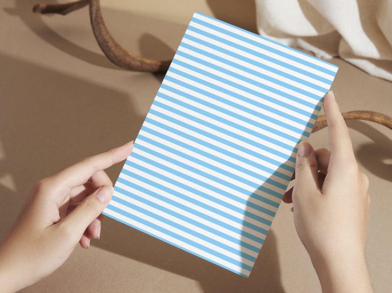 May include: A white card with blue horizontal stripes. The card is being held by a person's hands.