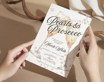 May include: A white invitation card with a watercolor illustration of two champagne flutes with pearls. The text on the card reads "Pearls & Prosecco" and "Please join us for a bridal shower honoring Nicole White, Saturday, March 9, 2PM".
