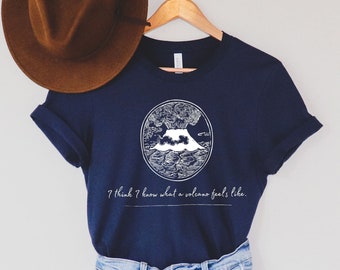 May include: A navy blue t-shirt with a white graphic of a volcano erupting. The text "I think I know what a volcano feels like" is printed below the graphic.