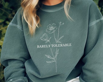 Puede incluir: Una sudadera verde oscuro con un diseño floral blanco y el texto "Barely Tolerable" impreso en la parte delantera.