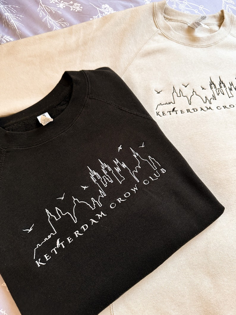 May include: Two sweatshirts with a skyline graphic and the text "Rotterdam Crow Club". The sweatshirt on the top is beige and the sweatshirt on the bottom is black.