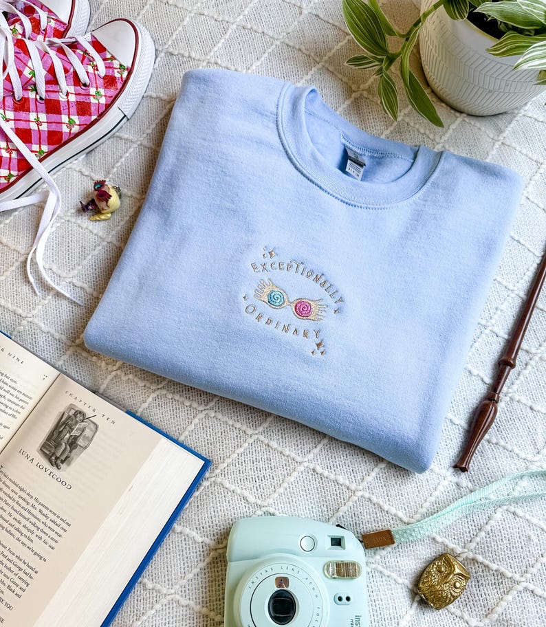 May include: A light blue sweatshirt with the text "Exceptionally Ordinary" and a pair of embroidered glasses with pink and blue lenses.