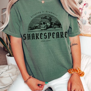 May include: A green t-shirt with a skull wearing a crown and the text "Keeping it dramatic Shakespeare since 1564".