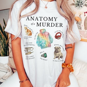 May include: White t-shirt featuring the text "Anatomy of a Murder" and various illustrations, including a cat, a tie-dye hoodie, headphones, a bulldog, and a ring. The text "Maybe we should do a Tie-Dye Guy podcast about Evelyn. This sends the investigation into a whole new direction. Who is Tim Kono?" is also on the shirt.