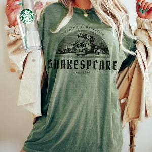 May include: A green t-shirt featuring a skull wearing a crown and holding a sword. The text on the shirt reads "keeping it dramatic Shakespeare since 1564".